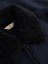 Close-up of the BGdugal Bomber Jacket - Dark Navy by Blue de Gênes, featuring a black, fuzzy sherpa teddy collar and a visible zipper. A small tan tag with the Blue de Gênes logo and text is partially visible inside the collar.
