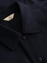 Close-up of the Blue de Gênes BGBoyd Wool Jacket in dark navy, featuring a pointed collar, fabric-covered buttons, and a beige label with a small shield logo inside the neckline. Inspired by durable workwear, this jacket blends timeless style with lasting resilience.