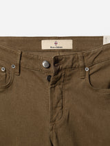 Close-up of beech green denim pants showing the waistband, front pockets, belt loops, metallic button, zip fly, and a label that reads Blue de Gênes with a small emblem above the text. Crafted from comfort stretch twill for ease of movement, these regular fit BGvinci Iro Pants by Blue de Gênes offer both style and everyday versatility.