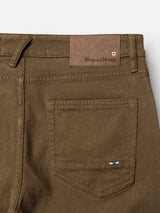 Close-up of the back pocket of beech green BGvinci Iro Pants by Blue de Gênes, crafted from comfortable stretch twill, featuring a small stitched flag and a leather patch with the Blue de Gênes logo on the waistband.
