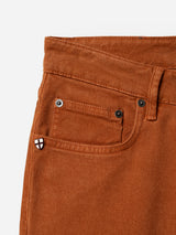 Close-up of the BGvinci Iro Pant in Ginger Bread Orange from Blue de Gênes, highlighting the waistband, front pocket, coin pocket with a small black and white shield-shaped pin, belt loop, button, and rivets. Crafted from comfort stretch twill for ease of movement, these regular fit jeans blend style and comfort in every detail.