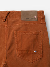 Close-up of the BGvinci Iro Pant in Ginger Bread Orange by Blue de Gênes, highlighting a back pocket, belt loops, and a brown leather patch featuring the brand’s logo along with a small red and white emblem. Crafted from comfort stretch twill, these regular fit pants combine style with flexibility.