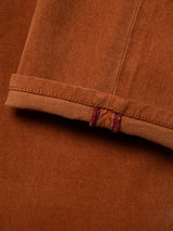 Close-up of the ginger bread orange fabric of the BGvinci Iro Pant by Blue de Gênes, featuring a folded edge with visible stitching and two short vertical red stitches near the hem. The texture highlights diagonal weave patterns characteristic of comfort stretch twill, commonly found in regular fit styles like these pants.