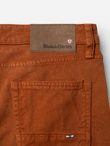 Close-up of the BGvinci Iro Pant in Ginger Bread Orange, highlighting a back pocket with a small blue and white tag and a brown leather label featuring the Blue de Gênes name and a red and white crest above the pocket. Crafted from comfort stretch twill, these pants combine style and flexibility for all-day wear.