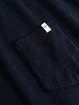 Close-up of the BGoscar T-Shirt in dark navy by Blue de Gênes, featuring slub cotton fabric and a chest pocket with a small white tag and red geometric logo sewn into the top right seam.
