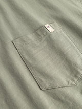 Close-up of the BGoscar T-Shirt - Shadow Green by Blue de Gênes, made from light green slub cotton. Features a neatly stitched chest pocket with a small beige tag near the top edge, highlighting signature detailing.