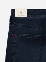 Close-up of the back pocket of BGgiacomo BB Jeans in Blue Black Denim by Blue de Gênes, made from rigid denim with a small red stitch detail, featuring a cardboard tag with the Blue de Gênes name and a red and white shield logo above it.