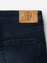 Rewritten sentence: Blue de Gênes BGgiacomo BB Jeans in blue black rigid denim, featuring a brown leather patch with a shield emblem on the waistband. The image displays the top section of these relaxed loose fit jeans, highlighting part of the back pocket and detailed stitching.
