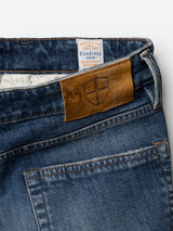 Close-up of the BGvinci Break Jeans in a dark blue denim wash from Blue de Gênes, featuring a brown leather patch with a shield logo above the back pocket and an interior white label reading "Candiani Denim" inside the waistband. Made from comfort stretch denim for easy movement and all-day comfort.