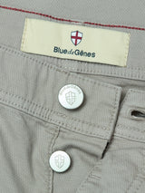 Close-up of shadow green BGpaulo Teo Pant by Blue de Gênes, featuring two branded metal buttons and a cream label with a red cross shield and “Blue de Gênes” text above the waistband.