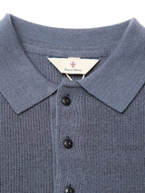 A close-up of the Porto Polo Knit in Dark Slate shows its textured blue fabric, collar, and black buttons. The white inner tag displays the Blue de Gênes brand, emphasizing this piece as refined luxury knitwear.