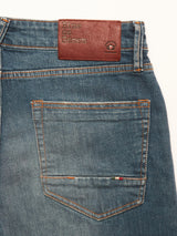 Close-up of the Vinci Topaz Vintage Jeans - Used by Blue de Gênes, featuring blue denim in a regular fit with a back pocket highlighted by orange stitching and a brown leather patch on the waistband stamped with the brand name. Crafted from comfort stretch denim and made in Italy.
