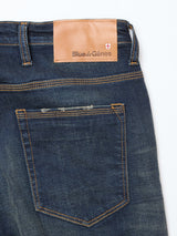 Close-up of the back of Repi Dark Vintage Jeans by Blue de Gênes in mid blue denim, featuring a branded leather patch above the right pocket, orange stitching, and slight fading for a vintage look.