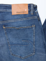 A close-up of Blue de Gênes Recco Blue Vintage Jeans in vintage wash shows the back with a single rear pocket, decorative stitching, and a brown leather patch on the waistband.