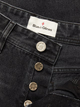 Close-up of a pair of Giacomo BLK Used Jeans in grey denim by Blue de Gênes, featuring metallic buttons and a label with the brand name. The jeans are partially unbuttoned to reveal the brand tag and button details, emphasizing the timeless appeal of classic rigid denim.