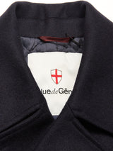 Close-up of a coat collar featuring a white label with a red shield and partial text rue de Gén. The label is stitched to the dark fabric of the Shiba Melton Coat - Dark Navy by Blue de Gênes, expertly crafted from premium Italian Melton wool.