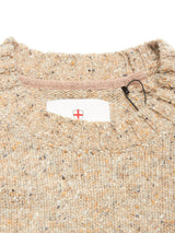 Close-up of the collar on the Honshu Crewneck Knit - Fungi, a beige, speckled chunky knit sweater by Blue de Gênes, with a white label featuring a partially visible red cross shield inside the neckline.