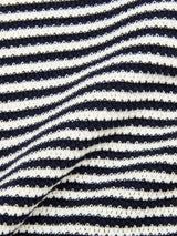 Close-up of the BGbob Knit Polo - Navy by Blue de Gênes shows its cotton knit fabric with navy and white stripes. A visible fold adds texture, emphasizing the classic look of this short-sleeve polo.