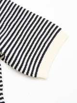 A detailed view of the BGbob Knit Polo - Navy by Blue de Gênes shows its black and white striped sleeve with a solid cream cuff. Made from 100% cotton, the shirt is displayed against a clean white background.