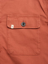 Close-up of the pocket on the BGpontus Teo Overshirt in Copper Brown by Blue de Gênes, showing its honeycomb cotton texture, a black button, and a small white tag with a red shield emblem sewn onto the left side of the pocket.
