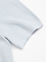 Close-up of the Filo Knit Polo in Blue Water by Blue de Gênes, a light blue short-sleeve knit with a textured waffle pattern and ribbed cuff, laid flat on a white background.