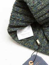 A close-up of the Oscar Melange Beanie - Forest by Blue de Gênes shows its textured, multicolored knit and a white label reading “80% Wool, 20% Recycled Nylon,” with a cardboard tag on a black string visible in the corner.