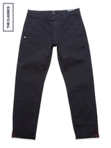 The Blue de Gênes Menzo Dobby Chino in dark navy features front and back pockets, button and zipper closure, and a logo patch by the right pocket. Laid flat on white with a THE CLASSICS label on the left.