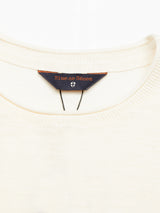 Close-up of the Monte Knit - Whitecap sweater’s off-white neckline, featuring a navy Blue de Gênes label with orange text and a small shield emblem beneath it.