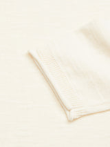 Close-up of the cuff of the Blue de Gênes Monte Knit - Whitecap, a cream-colored long-sleeve knit, laid flat on a matching cream fabric background.