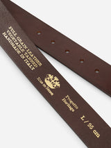 Close-up of the BGathol Belt - Dark Brown by Blue de Gênes, crafted from full-grain leather and stamped with gold text indicating it is handmade in Italy, vegetable-tanned, and size L/95 cm. Featuring a classic metal buckle and adorned with the crest logo alongside "Elue de Chapes" and "Progetto Heritage," this refined accessory epitomizes timeless style.