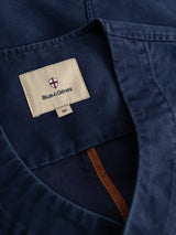 Close-up of the blue collar of the BGlumen Nebraska Gilet by Blue de Gênes, featuring a beige brand label with the Blue de Gênes name and a red, white, and blue shield logo. Below the main label is a size tag marked 50, emphasizing the brand’s attention to detail seen throughout their classic workwear and high-density cotton collections.