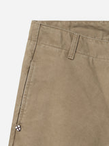 Close-up of the upper section of the BGliam Nebraska Chino - Brown by Blue de Gênes, highlighting the belt loop, front pocket, detailed stitching, and a small shield-shaped logo near the pocket. The subtle dobby weave enriches the brown cotton fabric with texture and depth.