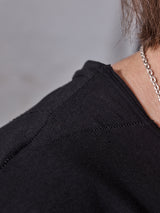 Close-up of a person’s shoulder and neck wearing the Blue de Gênes Sagi Nuovo T-shirt in black, paired with a silver chain necklace and part of their hair visible against a plain background.