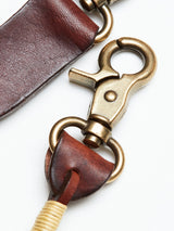 Close-up of a brass lobster clasp attached to dark brown leather, with a leather loop secured by wrapped beige thread at one end. The BGsavino Key Hanger - Brown from Blue de Gênes features sturdy hardware with an antique finish on genuine cow leather, blending durability with timeless design.
