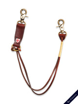 A brown leather hunting dog slip lead with brass snap hooks, a small red and white emblem, and a yellow-wrapped section is displayed against a white background with “The Classics” label in the lower right corner. For a coordinated look, pair it with our BGsavino Key Hanger - Brown from Blue de Gênes.