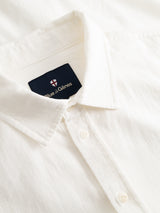 Close-up of a white, honeycomb-textured cotton button-up shirt with a collar. The shirt’s dark tag reads “Blue de Gênes” and features a small red and white cross logo. Shown: BGenrico Tessusto Shirt in Chalk.