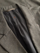 A close-up of the BGFukui Wool Blazer - Grey Mel by Blue de Gênes reveals its smooth dark lining and precise interior stitching. A small metallic shield pin accents the lapel, emphasizing this relaxed fit blazer’s refined attention to detail.