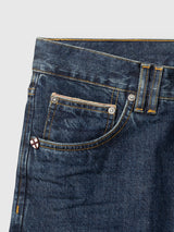 Close-up of the front pocket area of Blue de Gênes BGmarco Cast Jeans - Denim wash, crafted from blue cotton denim in a relaxed fit, featuring yellow stitching, a coin pocket, belt loops, and a small shield-shaped pin near the seam.