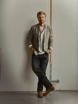 A man wearing a grey blazer, white shirt, patterned neck scarf, and BGmarco Connor Jeans - Black Denim Used leans against a wall.