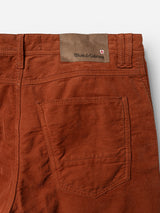 Close-up of the back of the BGpaulo Ottawa V3 Trousers in Ginger Bread Orange by Blue de Gênes, featuring a slim fit with a pocket and a brown leather patch above it embossed with the Blue de Gênes logo beside a small red and white shield emblem, crafted from textured dobby corduroy reminiscent of classic chino pants.