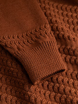 Close-up of a rust-orange BGstu Rollneck Knit - Ginger Bread Orange sweater sleeve featuring a textured cable-knit pattern and a ribbed cuff.