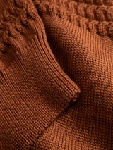 Close-up of a burnt orange BGstu Rollneck Knit - Ginger Bread Orange 100% wool sweater featuring a textured cable-knit pattern on the shoulder and a ribbed cuff.