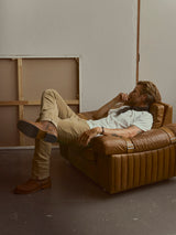 A man in a white t-shirt and slim fit Blue de Gênes BGpaulo Ottawa V3 Trousers in sepia tint brown relaxes in a leather armchair.