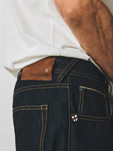 Close-up of rigid dark denim Blue de Gênes BGgiacomo Selvedge V3 Jeans in a relaxed loose fit, featuring a brown leather back patch and contrast stitching.
