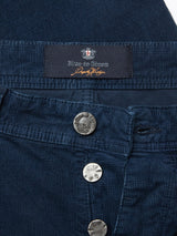 Close-up of a pair of navy Paulo Tucan Chinos by Blue de Gênes. Made in Italy, featuring a metal button with the brands logo above a row of others, showcasing the comfort stretch fabric texture and design details.