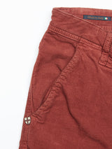 Close-up of the rust-colored Paulo Tucan Chino - Chipotle from Blue de Gênes, with visible stitching, side pocket, and a small shield-shaped badge near the pocket. Tag displays Made in Italy with Italian flag colors. Pants are laid flat on a pristine white background.