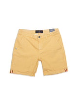 The Teo Milano Shorts by Blue de Gênes are sand-colored chino shorts in a cotton/linen blend with button and zip closure, side pockets, red and gray tag details at the hem, a subtle textured fabric, and a belt loop waistband.