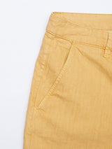 Close-up of Teo Milano Shorts - Sand by Blue de Gênes on white background, highlighting a single side pocket, belt loop, and seam details. The mustard-colored fabric appears to be a cotton/linen blend, exuding relaxed elegance.