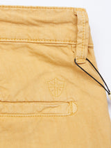 Close-up of a mustard fabric pocket on the Teo Milano Shorts - Sand from Blue de Gênes features a stitched shield emblem and a thin black cord, showcasing quality craftsmanship typical of chino shorts in a cotton/linen blend.