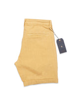 Sand Teo Milano Shorts by Blue de Gênes are neatly folded to showcase a visible back pocket and button closure. Made from a comfortable cotton/linen blend, they feature a tag attached at the waist.